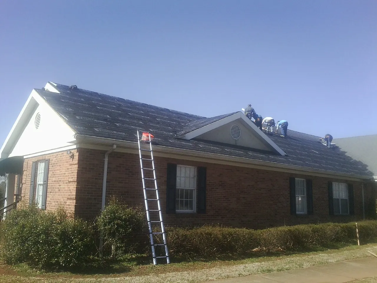 Crew tearing shingles off a brick ranch roof with a ladder set — Emergency Roof Repair work by our crew in Ashley