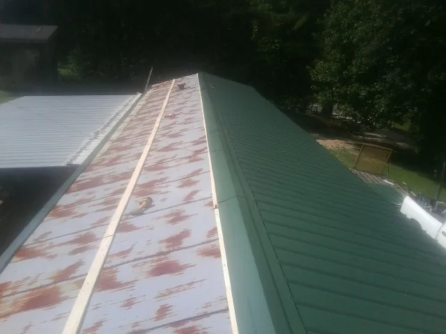 Old rusted panels beside newly installed green metal roofing — Wind Damage Roof Repair by Roofing Brothers in Ashley
