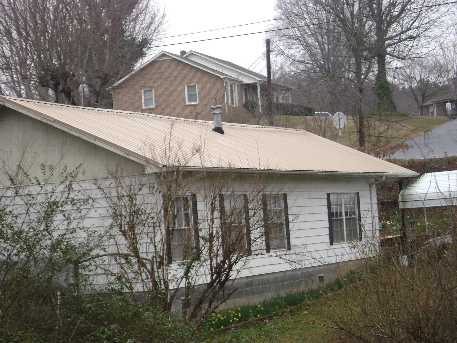 Tan metal roof on a white sided house set into a hillside — Commercial Roofing by Roofing Brothers in Ashley